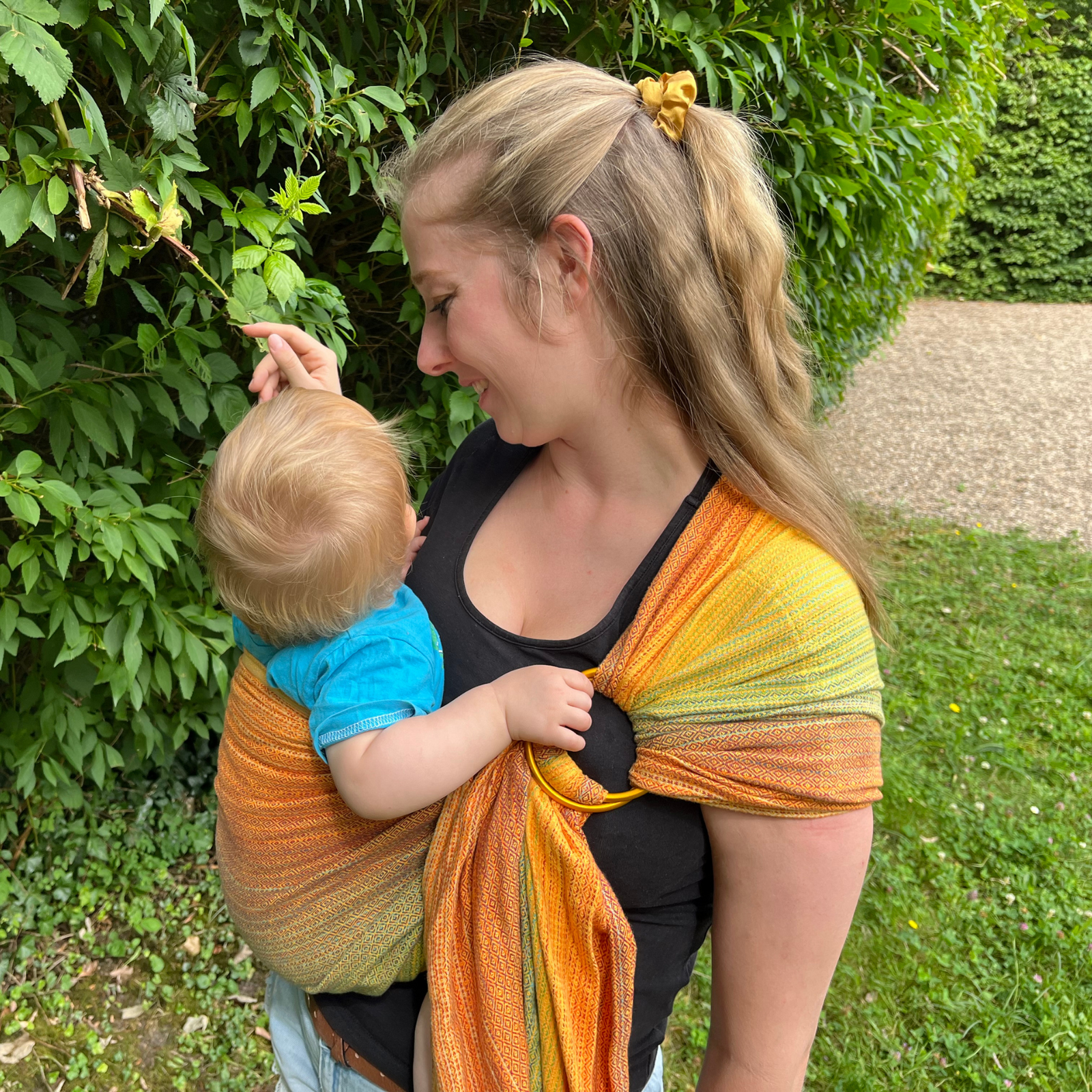 Ringsling Free Elf fusion d'oro double weft Tragebild mit Baby und Mama vor einer grünen Hecke